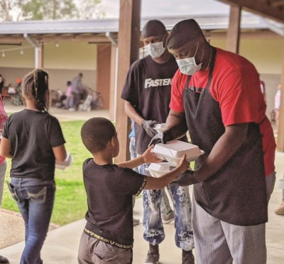 Masked volunteers hand a packaged meal to a small child