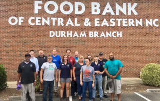 Group of 15 Durham branch staff members gather in matching food bank shirts in front of the Durham Branch building. 