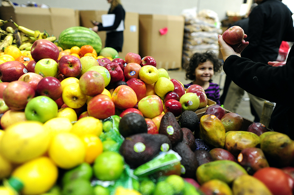 Girl smiles next to someone taking an apple from a large produce display