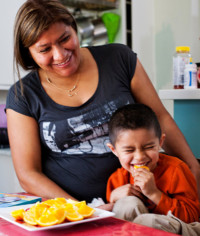 Woman and child sitting together laughing, the child with an orange slice