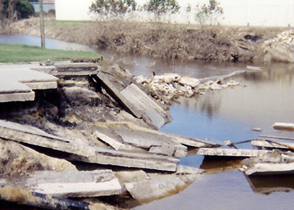 A bridge broken into pieces scattered around a river bank. 