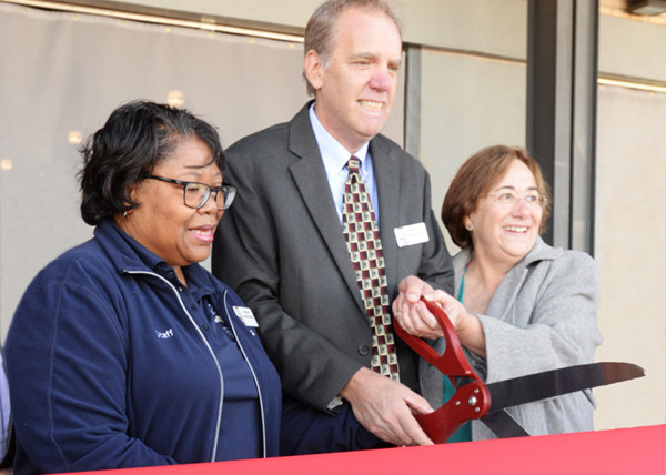 President and CEO with 2 staff cut a large red ribbon with oversized scissors