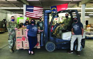 Masked members of Wilmington Branch Staff and the National Guard pose around a forklift loaded with boxes of apples.