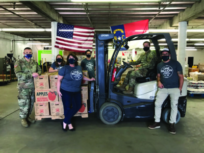 Masked members of Wilmington Branch Staff and the National Guard pose around a forklift loaded with boxes of apples. 