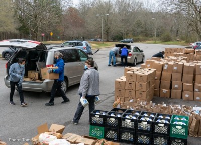 Masked volunteers load a van with boxes from a stack to the right at a drive through distribution
