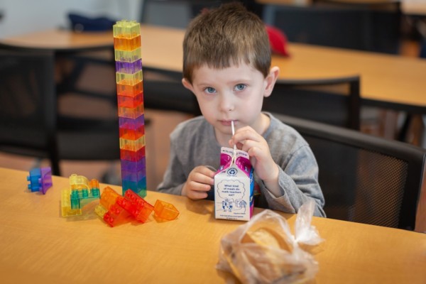 Little boy drinking milk from a carton next to a tall tower of lego bricks