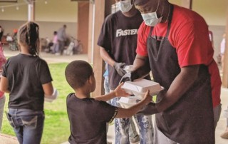 Masked volunteers hand a packaged meal to a small child